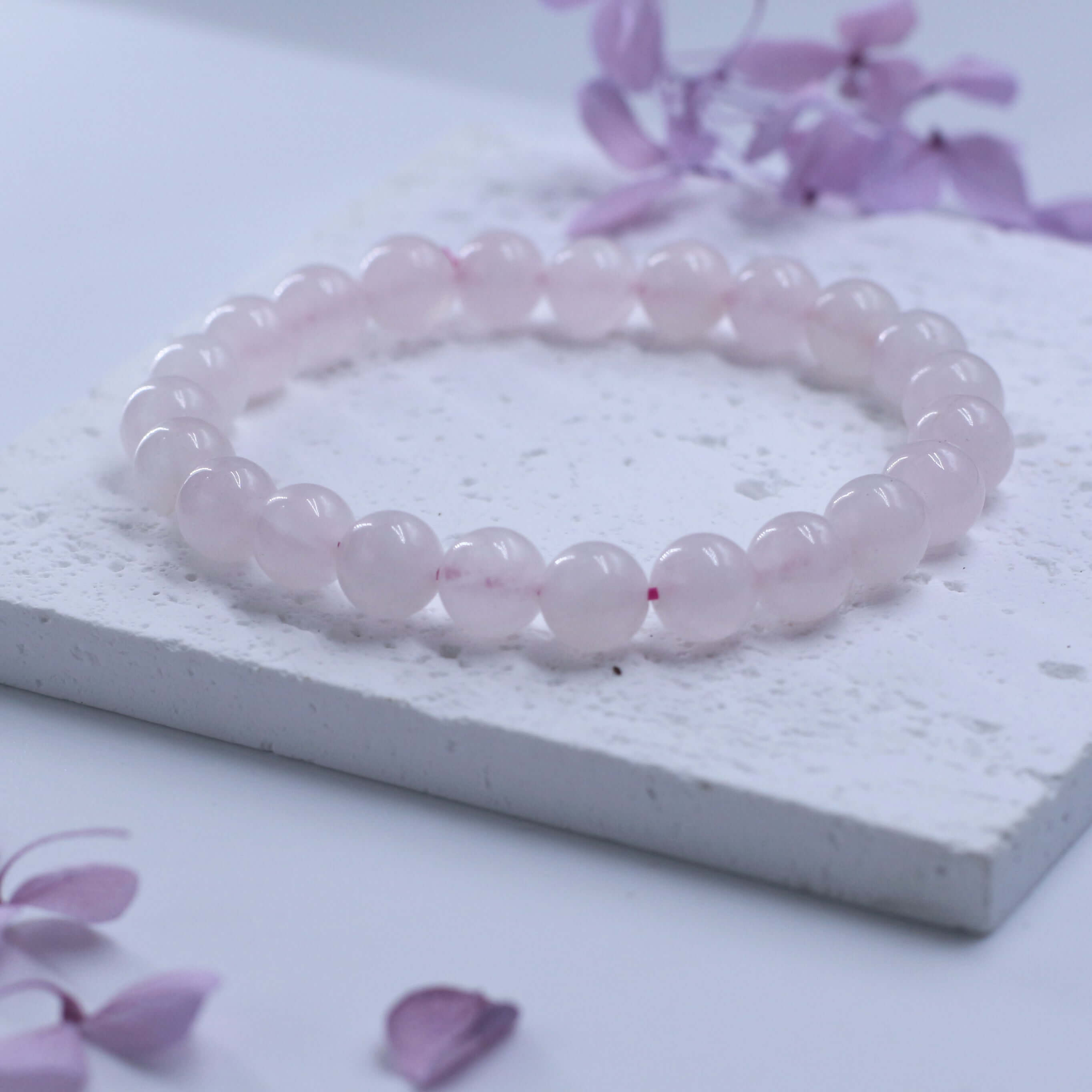 Romantic Rose Quartz Bracelet - Love on white surface with purple petals, symbolizing love and healthy relationships.