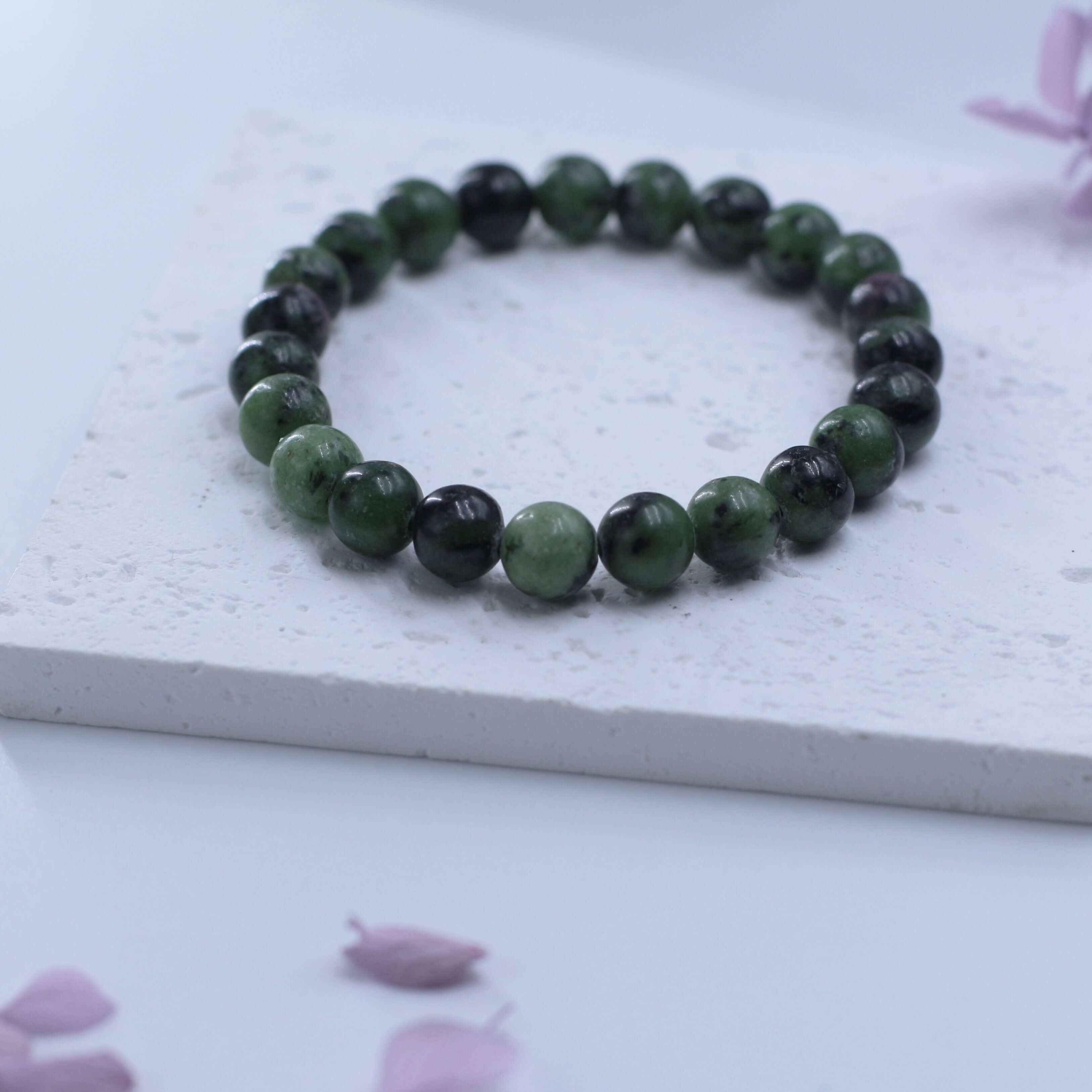 Mysterious zoisite bracelet with deep red-green beads on a textured white surface, ideal for spiritual seekers.