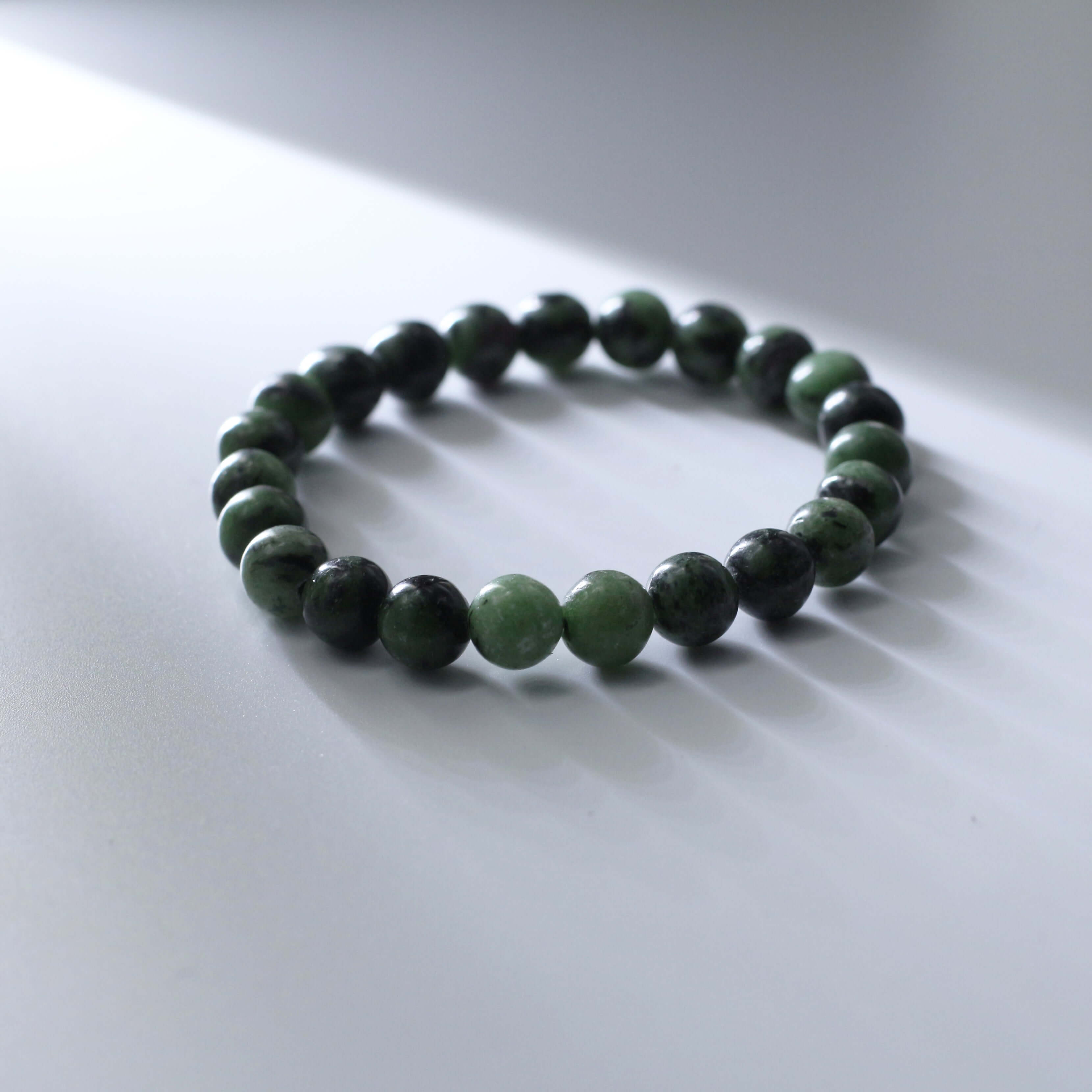 Mysterious zoisite bracelet with deep red-green hue beads showcasing natural texture on a light surface.