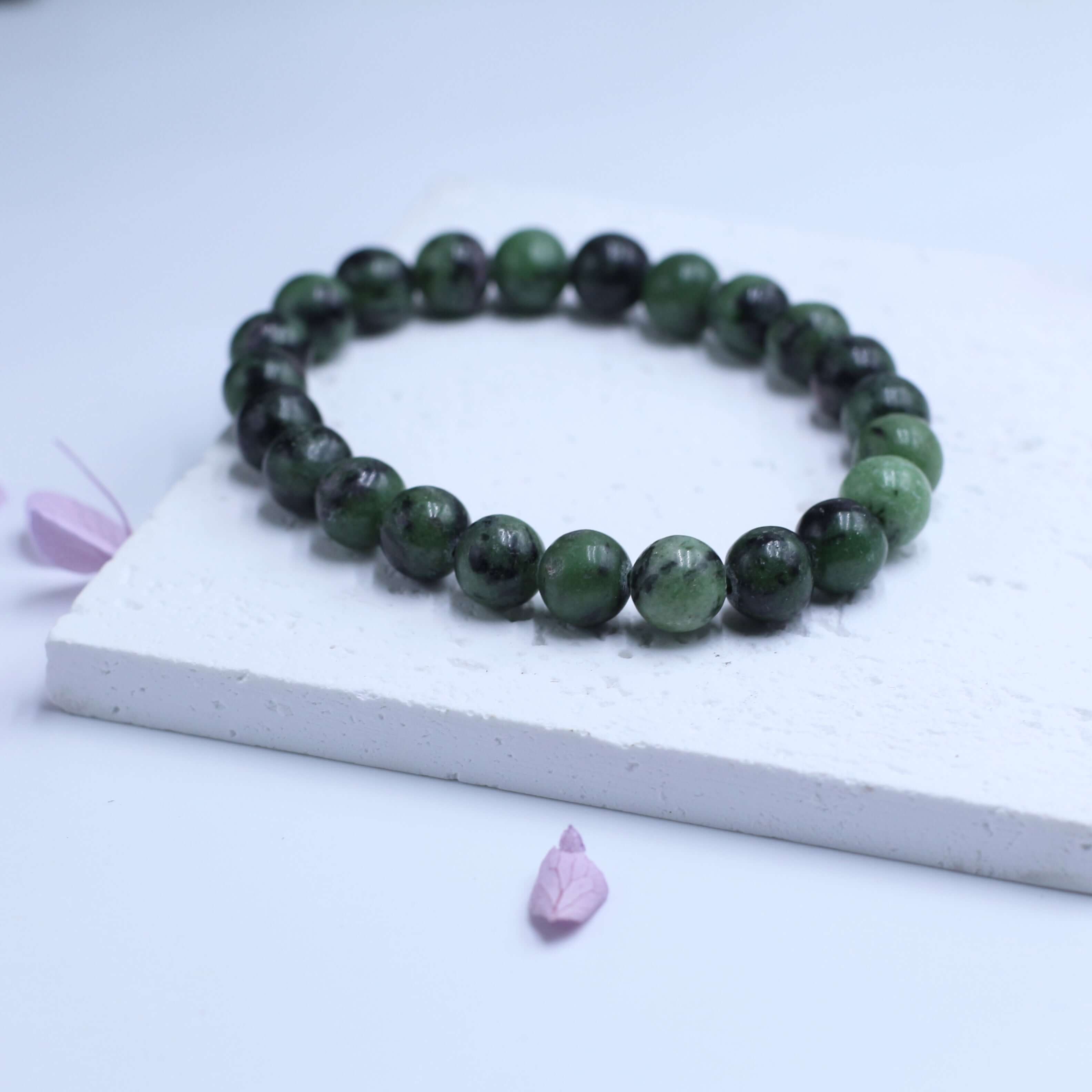 Zoisite bracelet with deep red-green hues on white platform, embodying spiritual wisdom and mystery.