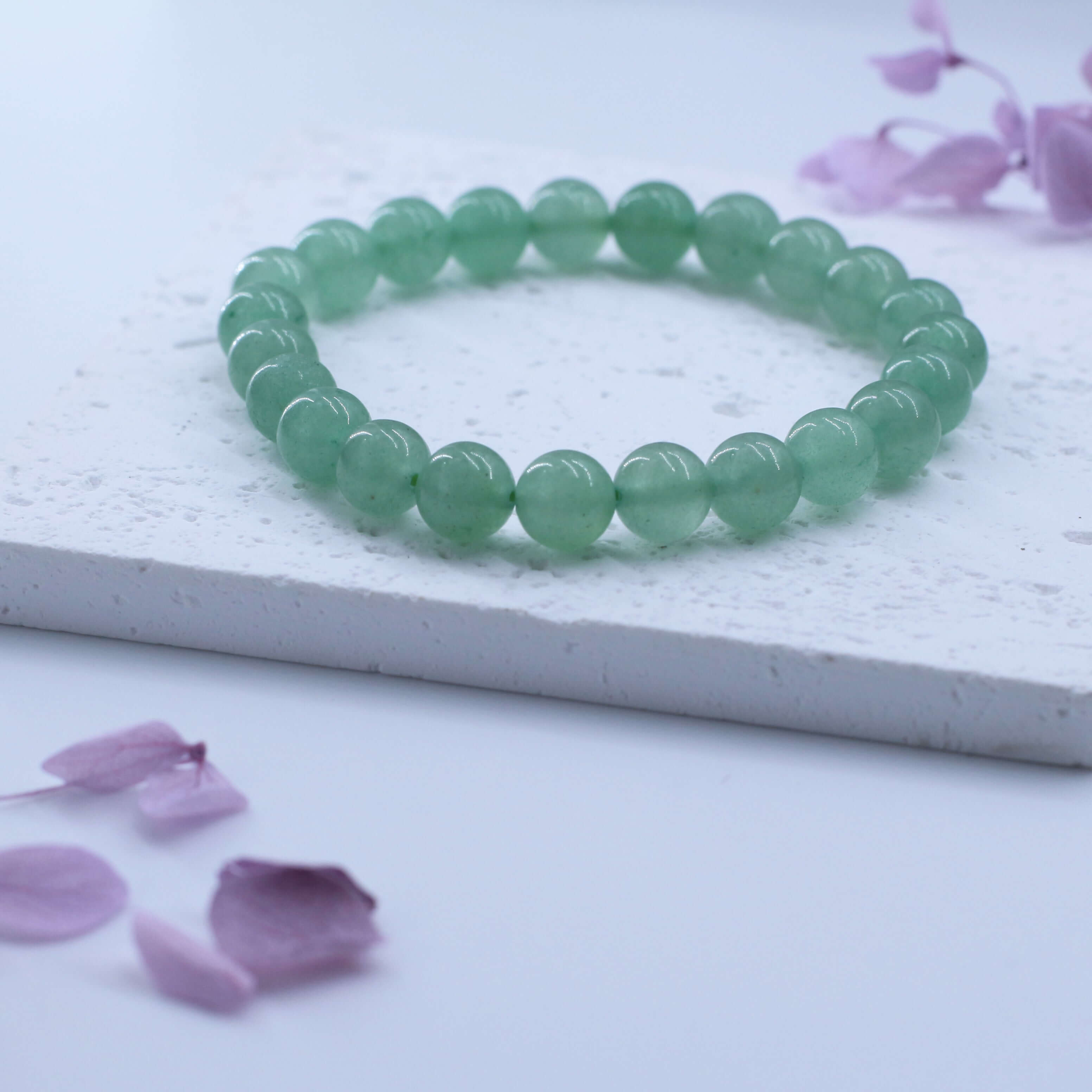 Natural Green Aventurine Bracelet promoting health and vitality, displayed on a textured white surface with purple petals.