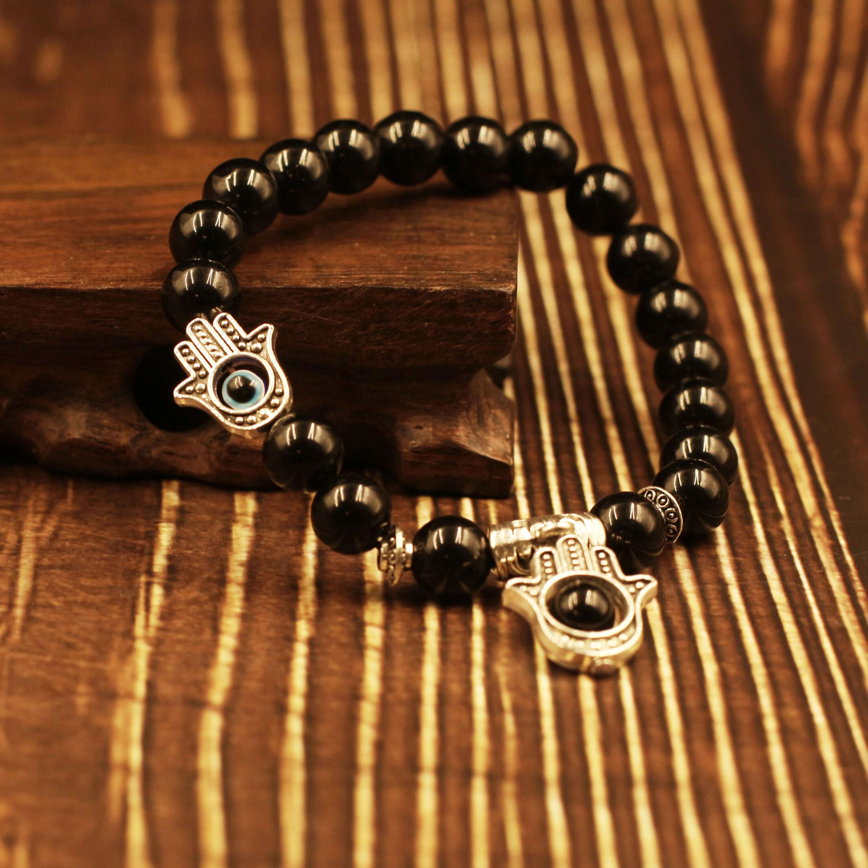 The Eye of Horus Bracelet-Health & Insight with black beads and silver charms on wooden background.