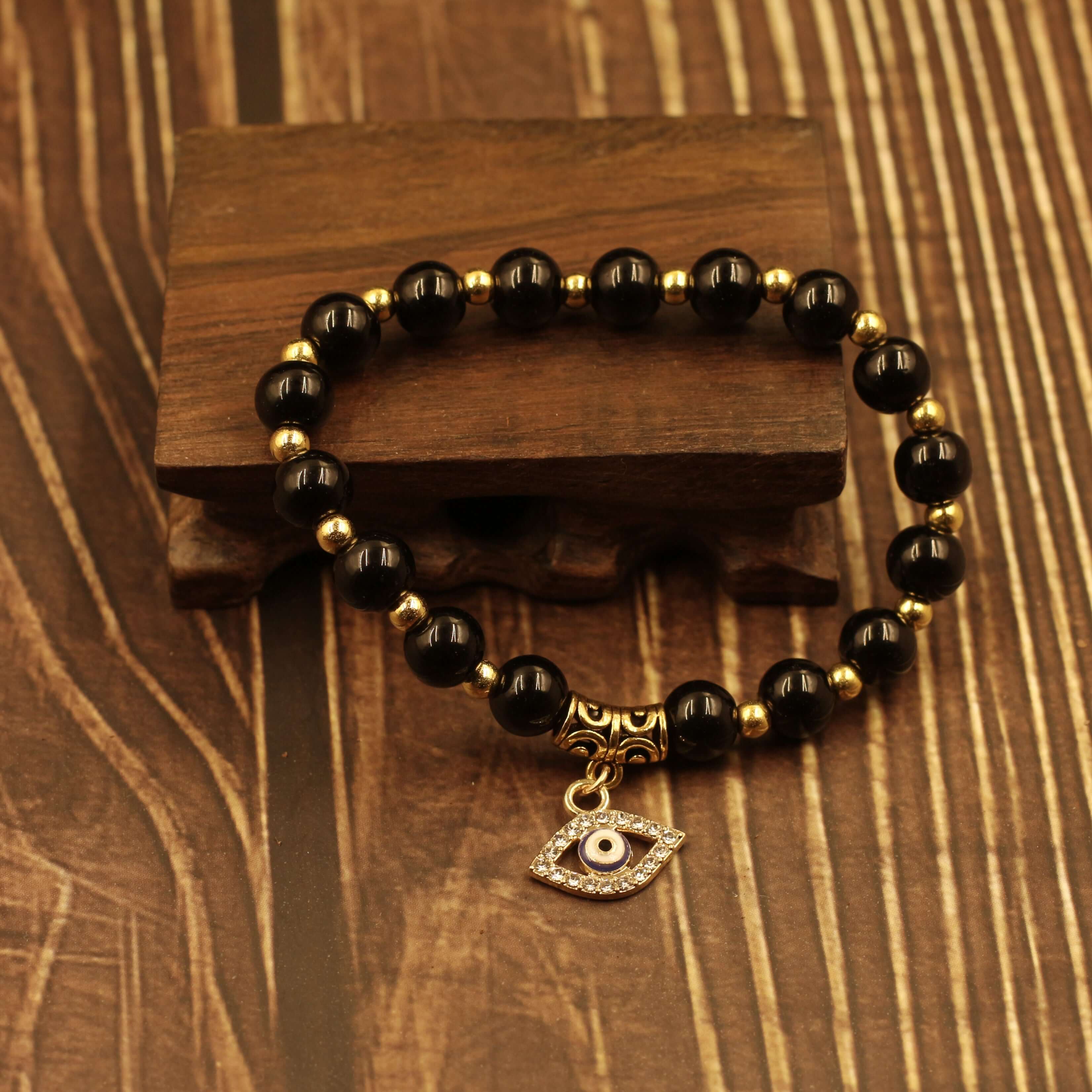 Evil Eye Bracelet-Protection with black beads and gold accents displayed on wooden background.