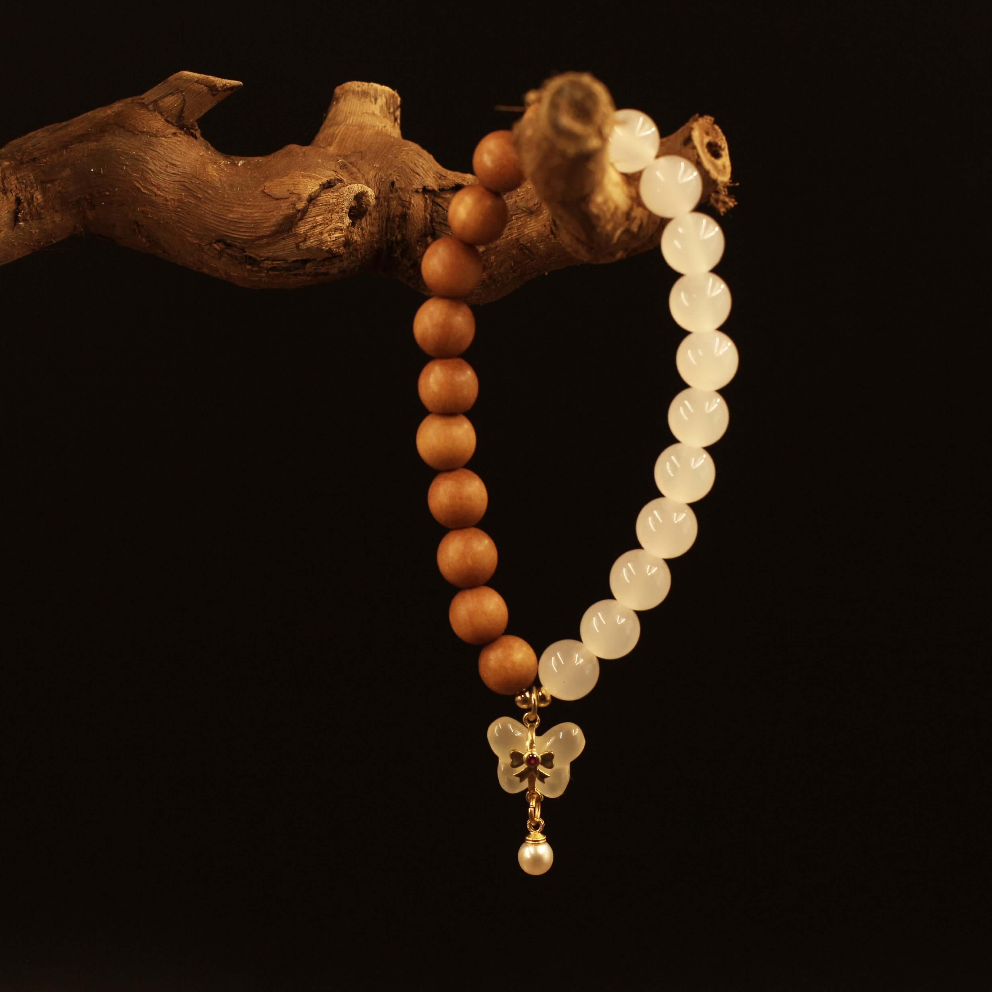 Double Purifying Butterfly Tassel Bracelet with sandalwood beads for clarity and new life, displayed on a wooden branch.