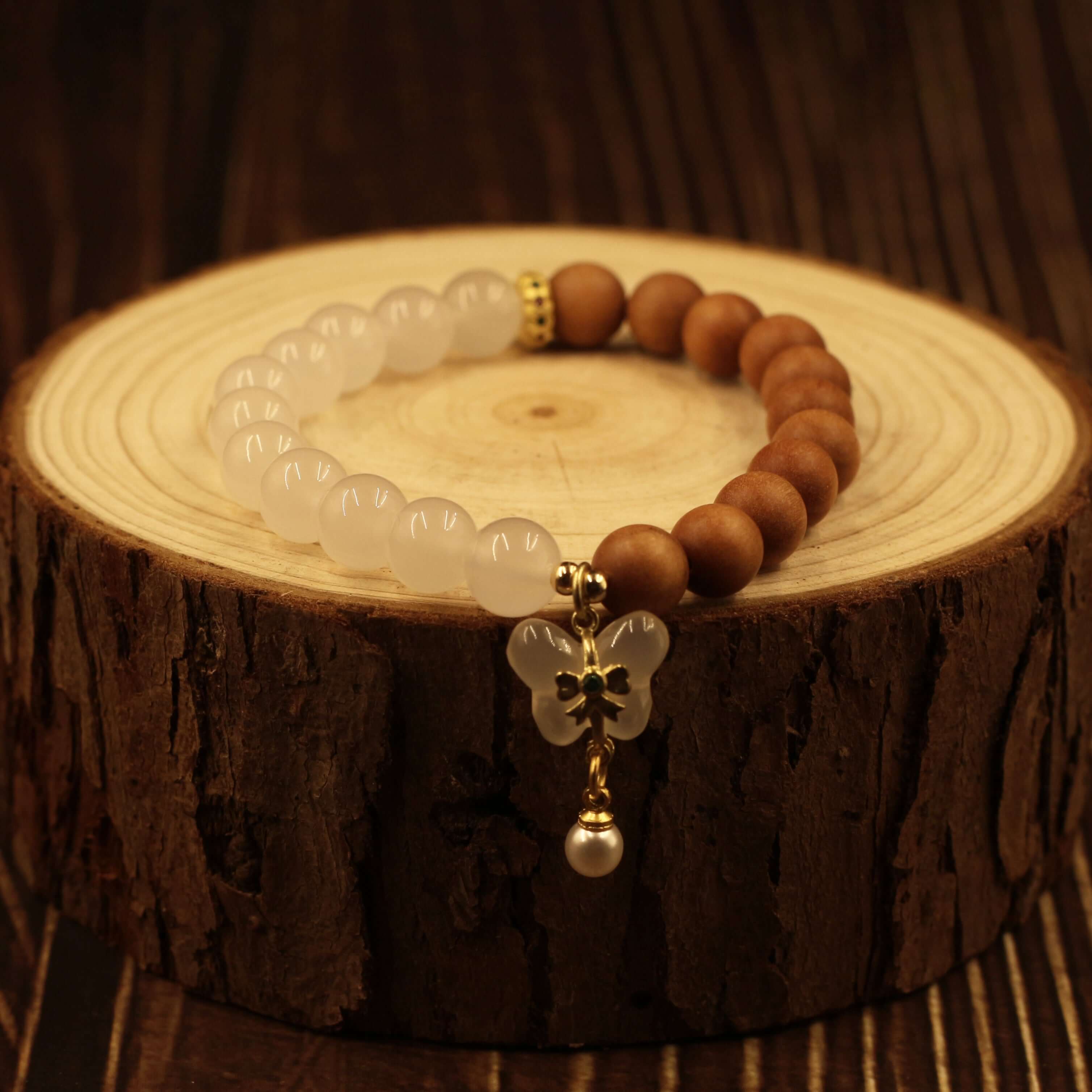 Double Purifying Butterfly Tassel Bracelet with sandalwood and beads for clarity and new life displayed on wooden surface.