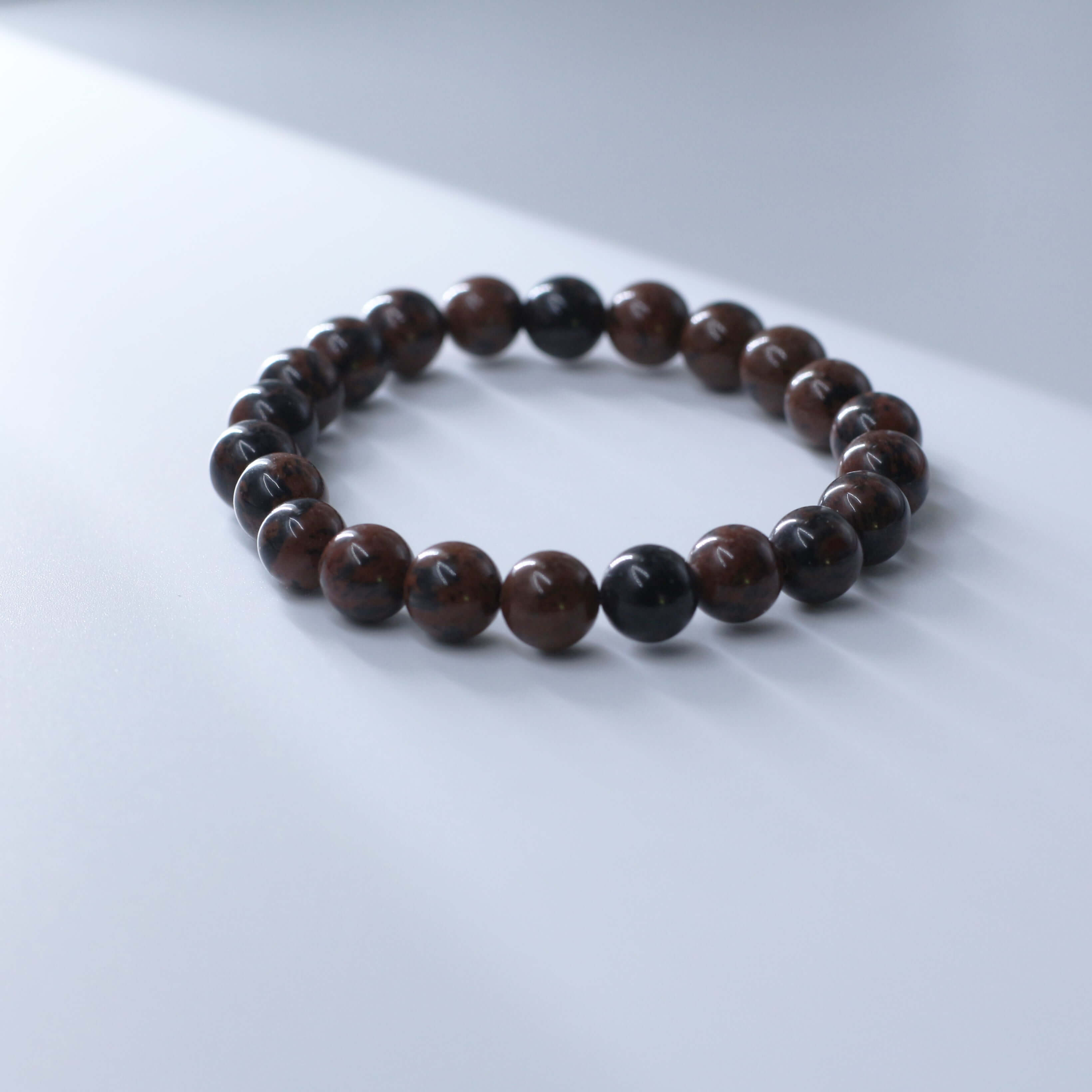 Flame Red Tiger's Eye Bracelet for courage and spiritual growth, featuring polished brown beads in a serene setting.